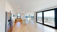 Located at The Breeze on Long Beach's iconic Boardwalk, this thoughtfully designed 2-bedroom, 2-bathroom residence offers an exceptional coastal living experience. The open-concept kitchen and living area is the heart of the home, featuring light wood-tone flooring throughout, recessed lighting, and striking floor-to-ceiling sliding glass doors that open onto a private balcony with unobstructed ocean views. The kitchen is appointed with two-tone cabinetry, white quartz countertops, stainless steel appliances including a built-in microwave, and pendant lighting over a central island. The spacious primary bedroom is bathed in natural light, framed by large black-trimmed windows showcasing panoramic views of the Atlantic. The second bedroom also benefits from generous windows with open skyline views. Both bathrooms are finished with large-format tile flooring, floating vanities with quartz surfaces, LED-backlit mirrors, and glass-enclosed showers. A stacked Whirlpool washer and dryer are conveniently located within the unit. Two closets provide ample storage. Clean lines, a neutral palette, and an abundance of natural light give the entire residence a bright, modern, and airy coastal ambiance.