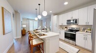 This thoughtfully designed one-bedroom, one-bathroom residence offers an efficient and stylish single-floor layout. The open-concept kitchen and living area serves as the heart of the home, featuring crisp white shaker cabinetry, a subway tile backsplash, stainless steel appliances — including a range, microwave, and French-door refrigerator — and a generous island with a stainless steel sink and bar seating for multiple guests. Globe pendant lights add a modern touch overhead, while light wood flooring flows throughout. The adjacent living room receives abundant natural light through large windows and glass doors, and includes a ceiling fan for added comfort. The bedroom is a calm retreat finished in soft sage tones, with plush carpeting, a ceiling fan, and a sizable window offering outdoor views. It connects directly to the full bathroom, which features a dual-sink vanity with white cabinetry, a deep soaking tub, and a sleek tiled shower surround. The walk-in closet provides ample storage with built-in shelving and hanging rods, and conveniently houses a stacked washer and dryer unit. A hallway completes the functional layout of this well-organized residence.