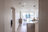 This thoughtfully designed single-floor residence combines clean, modern aesthetics with practical functionality throughout. A welcoming entry corridor, finished with light wood-toned flooring and crisp white walls, leads naturally into the heart of the home. An electrical panel is conveniently accessible near the entry, and ceiling-mounted HVAC vents ensure efficient climate control throughout the space.

The kitchen is a standout feature, outfitted with stainless steel appliances including a gas range, built-in microwave, and a French door refrigerator with an ice and water dispenser. Light wood cabinetry extends to the ceiling, offering generous storage, while white lower cabinets and a white quartz countertop create a bright, contemporary contrast. A tile backsplash and a deep stainless steel sink with a pull-down faucet complete the well-appointed workspace.

The bedrooms are bright and airy, benefiting from large, floor-to-ceiling windows with black frames that invite natural light and offer views of surrounding greenery. The light hardwood flooring extends seamlessly throughout, enhancing the sense of openness.

The bathroom is finished in light neutral tones, featuring large-format tile flooring, a wood-grain vanity with white countertop, an illuminated mirror, and an open roll-in shower area with grab bars, reflecting accessible design considerations. The overall ambiance of the residence is calm, clean, and move-in ready.