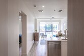 This thoughtfully designed single-floor residence combines clean, modern aesthetics with practical functionality throughout. A welcoming entry corridor, finished with light wood-toned flooring and crisp white walls, leads naturally into the heart of the home. An electrical panel is conveniently accessible near the entry, and ceiling-mounted HVAC vents ensure efficient climate control throughout the space.

The kitchen is a standout feature, outfitted with stainless steel appliances including a gas range, built-in microwave, and a French door refrigerator with an ice and water dispenser. Light wood cabinetry extends to the ceiling, offering generous storage, while white lower cabinets and a white quartz countertop create a bright, contemporary contrast. A tile backsplash and a deep stainless steel sink with a pull-down faucet complete the well-appointed workspace.

The bedrooms are bright and airy, benefiting from large, floor-to-ceiling windows with black frames that invite natural light and offer views of surrounding greenery. The light hardwood flooring extends seamlessly throughout, enhancing the sense of openness.

The bathroom is finished in light neutral tones, featuring large-format tile flooring, a wood-grain vanity with white countertop, an illuminated mirror, and an open roll-in shower area with grab bars, reflecting accessible design considerations. The overall ambiance of the residence is calm, clean, and move-in ready.