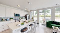 This contemporary two-bedroom, two-bathroom residence in St. Francis, Wisconsin offers a thoughtfully designed single-floor layout with clean architectural lines and a bright, modern aesthetic. The open-concept kitchen is a standout feature, showcasing floor-to-ceiling windows that flood the space with natural light and offer outdoor views of the surrounding greenery. White shaker cabinetry, a tile backsplash, stainless steel appliances, and a generous island with bar seating create an inviting and functional culinary space. Light-toned wood-look flooring flows seamlessly throughout, complementing the home's crisp, neutral palette. The living area benefits from the same expansive glazing, reinforcing the airy, open feel. The spacious primary bedroom features large windows, a ceiling fan, and access to a walk-in closet with built-in wire shelving. The primary bathroom offers an extended vanity with a wood-framed mirror and tile flooring. The second bedroom is well-proportioned and equally light-filled. A second full bathroom includes a tub/shower combination and a white vanity. Throughout the residence, the design emphasizes clean lines, natural light, and a calm, contemporary atmosphere.