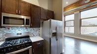 Located at 31 Barker St in Buffalo, NY, this two-bedroom, one-bathroom loft-style residence blends industrial character with modern finishes across a single floor. Exposed brick walls and large multi-pane windows are recurring architectural elements throughout, flooding the space with natural light and offering views of the surrounding Buffalo streetscape.

The living room is an open, airy space anchored by rich dark hardwood flooring, exposed brick accents, and a striking bank of floor-to-ceiling windows that frame the city outside. The kitchen is well-appointed with dark espresso cabinetry, light countertops, a mosaic tile backsplash, and a full suite of stainless steel appliances including a gas range, built-in microwave, dishwasher, and side-by-side refrigerator with water dispenser.

The two bedrooms feature plush carpeting and neutral tones. The primary bedroom offers a comfortable footprint with exposed brick and a large window, while the second bedroom maintains a similar cozy aesthetic. The bathroom is finished with large-format tile flooring and includes a glass-enclosed walk-in shower. Two hallways connect the rooms efficiently, completing the functional layout of this character-rich urban residence.