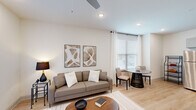 This thoughtfully designed one-bedroom, one-bathroom residence in Scott, Louisiana offers a cohesive open-concept layout with modern finishes and consistent light wood flooring throughout. The kitchen is a standout feature, boasting gray shaker-style cabinetry, granite countertops, a full suite of stainless steel appliances, and a spacious island with bar seating — ideal for both cooking and casual dining. The kitchen flows seamlessly into the living and dining area, which is bathed in natural light from large windows dressed with white blinds and curtains. A sliding glass door in the living room provides additional light and outdoor access. The bedroom is a comfortable retreat, featuring a ceiling fan, ample natural light from dual windows, and direct access to a walk-in closet with built-in shelving. The bathroom connects conveniently to the bedroom and includes a granite-topped vanity with gray cabinetry, a large mirror, and light wood flooring that continues from the rest of the unit. Recessed lighting and ceiling fans are found throughout, contributing to a bright, airy ambiance. The clean, neutral color palette and modern design elements create a polished and functional living space.