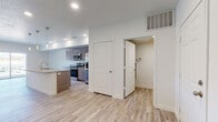 This single-floor space offers a clean, modern aesthetic defined by light wood-style flooring, crisp white walls, and recessed lighting throughout. The open-concept kitchen serves as a centerpiece, featuring warm wood-toned cabinetry, speckled granite countertops, and a full suite of stainless steel appliances including a range, microwave, and French door refrigerator. A spacious kitchen island with a built-in sink and pendant lighting above adds both functionality and style, seamlessly connecting the kitchen to the living area. The layout flows naturally into a bright living space anchored by a sliding glass door that invites natural light and provides direct access to an outdoor area with greenery views. The bedrooms are well-proportioned and comfortable — one features a ceiling fan and a large window with blinds offering outdoor views, while another opens to the exterior via sliding glass doors. The bathroom is finished with matching granite countertops, wood-toned vanity cabinetry, and a full soaking tub and shower combination with brushed nickel fixtures. A utility closet with additional storage adds practical convenience. The overall ambiance is bright, fresh, and move-in ready, with consistent finishes that lend the space a cohesive, contemporary feel.