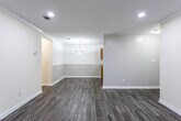Located at 875 Garden Walk Blvd in Atlanta, Georgia, this single-floor unit offers a clean, modern interior with a thoughtfully designed layout. The open living and dining area is finished with sleek gray wood-look flooring and neutral walls, creating a bright and versatile space. Recessed lighting throughout provides consistent illumination, while windows with white blinds allow natural light to filter in. Crown molding adds a refined touch to the main living area.

The living space flows naturally toward a dining area accented by a pendant light, which connects seamlessly to the kitchen. The kitchen is equipped with warm wood cabinetry, granite-style countertops, a double-basin sink, and black appliances including a refrigerator, dishwasher, and range. A window above the counter brings in additional natural light.

The bedroom offers plush carpeting underfoot, a ceiling fan with light fixture, and a window with blinds, creating a comfortable and restful environment. The bathroom features a granite-style vanity countertop with wood cabinetry and dark tile flooring, complemented by a dedicated laundry closet with hookups and shelving — a practical and space-efficient addition. The overall design is clean, neutral, and move-in ready.