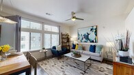 This single-floor residence is thoughtfully designed with a cohesive contemporary aesthetic carried consistently across each room. The living area serves as the heart of the space, benefiting from large windows fitted with horizontal blinds that draw in generous natural light. A ceiling fan anchors the room overhead, while hardwood-style flooring adds warmth underfoot. The layout comfortably accommodates a full seating arrangement, and wall space is well utilized with large-scale abstract artwork that introduces bold tones of blue, teal, and yellow — a color palette echoed throughout the residence.

The kitchen is outfitted with dark espresso cabinetry paired with granite countertops and a full suite of stainless steel appliances, including a dishwasher, range, and microwave. The design is practical and streamlined, offering ample storage and counter space.

The bedroom is a calm, well-proportioned retreat with neutral walls and soft carpeting. Artwork above the bed and bold accent pieces maintain the home's design continuity, creating a polished and cohesive feel.

The bathroom features large-format tile flooring, a glass-enclosed walk-in shower, a granite-topped vanity, and wall-mounted cabinetry, delivering a clean and functional space with modern detailing throughout.