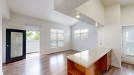 Located in Denver's Central Park neighborhood, this single-floor residence at 2871 Syracuse St offers a well-designed open-concept layout finished with warm wood-tone details and crisp white walls throughout. The living area benefits from vaulted ceilings that lend a sense of generous vertical space, while multiple windows fitted with horizontal blinds allow natural light to fill the room and provide views of surrounding greenery. A sliding glass door further connects the living area to the outdoors.

The kitchen is positioned as a central feature of the shared living space, anchored by a peninsula with a light stone-patterned countertop and open lower shelving. Warm wood cabinetry lines the walls above a tile backsplash, complemented by stainless steel appliances including a refrigerator, range, and microwave. Recessed lighting illuminates the cooking area effectively.

The bedroom is bright and well-proportioned, featuring two windows on adjacent walls that invite natural light from multiple directions. The room connects to a walk-in closet and an additional storage area. The bathroom is clean and functional, featuring a wood-framed vanity with a granite-style countertop, a large mirror, built-in niche shelving, and a tiled soaking tub and shower combination. Wood-look flooring runs consistently throughout the space, reinforcing the cohesive, contemporary aesthetic.