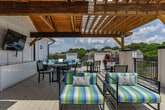 Located along Atlanta Student Movement Boulevard SW in Atlanta, Georgia, this rooftop terrace offers an inviting outdoor retreat designed for both relaxation and social gatherings. The space is thoughtfully divided into distinct seating areas, each serving a unique purpose while maintaining a cohesive aesthetic throughout.

A partially covered lounge area anchors one side of the terrace, featuring exposed wood beam ceiling accents that add warmth and architectural character. This shaded zone is furnished with a generously sized sectional sofa in teal upholstery, complemented by colorful striped accent chairs and a central fire pit table — creating an ideal setting for casual conversation and evening gatherings.

Adjacent to the lounge, an open-air dining area provides a round table with seating for multiple guests, bathed in natural sunlight and framed by vibrant potted flowers that add a lively pop of color. Light-toned tile flooring extends across the entire terrace, reflecting sunlight and contributing to the bright, airy atmosphere.

The terrace is enclosed by sleek black metal railings, offering unobstructed panoramic views of the Atlanta skyline, lush tree canopies, and the surrounding residential community. Built-in cabinetry with a stone countertop provides additional functionality along one wall. The combination of open sky, greenery, and thoughtful furnishings makes this rooftop terrace a standout feature of the property.