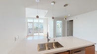 This contemporary single-floor residence showcases a clean, modern design with an open-concept layout that seamlessly connects the kitchen, dining, and living areas. The kitchen is well-appointed with warm wood cabinetry, quartz countertops, a large undermount stainless steel sink, a gas range with a geometric tile backsplash, a stainless steel French door refrigerator, and pendant lighting that adds a refined touch. The expansive living area features light hardwood flooring throughout and is anchored by a striking stone-surround fireplace, creating a welcoming focal point. Large floor-to-ceiling windows and glass doors flood the space with natural light and provide views of the surrounding neighborhood. The bedrooms are carpeted and generously sized, with multiple windows capturing abundant daylight and exterior views, and include built-in closet storage. The bathrooms are finished in a minimalist style, featuring large-format tile flooring, frameless glass shower enclosures, white subway tile, and floating vanities with undermount sinks and clean-lined fixtures. Throughout the residence, a consistent palette of white walls, neutral tones, and quality finishes creates a bright, cohesive, and sophisticated atmosphere ideal for modern living.