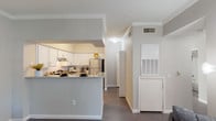 Located at 11355 Richmond Ave in Houston, TX 77082, this single-floor residence offers a thoughtfully designed layout that balances functionality and comfort. The open-concept kitchen is a standout feature, equipped with white shaker-style cabinetry, granite-style countertops, a subway tile backsplash, and stainless steel appliances including a refrigerator and electric range. A peninsula breakfast bar connects the kitchen to the main living area, creating an ideal space for casual dining and entertaining. Crown molding and dark hardwood-style flooring carry throughout the main living areas, lending a cohesive and polished look. The living room is bright and welcoming, featuring multiple windows with exterior door access that bring in natural light and provide outdoor connectivity. The bedroom is a calm retreat with carpeted flooring, vaulted ceilings, and a spacious walk-in closet. The bathroom is generously sized, showcasing white cabinetry, dual vanity mirrors, stone-look countertops, and a large vanity with ample storage. A dedicated in-unit laundry area adds everyday convenience. Overall, the space presents a clean, neutral palette with modern finishes throughout.