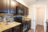 Located at 730 Franklin Rd SE in Marietta, Georgia, this single-floor residence offers a well-organized and functional layout designed for comfortable everyday living. The open living area features plush carpeting and neutral gray walls, creating a clean, versatile backdrop. A pass-through window connects the living space to the kitchen, enhancing the sense of openness and communication between rooms. The kitchen is thoughtfully appointed with rich dark cabinetry, granite-style countertops, black appliances including a range and over-the-range microwave, and a striking mosaic tile backsplash that adds a contemporary touch. Wood-look vinyl flooring runs through the kitchen and entry areas, providing durability and visual warmth. The bedrooms are carpeted and filled with natural light courtesy of large windows with blinds, lending each room a bright and airy feel. The bathroom features a dark vanity with granite-style countertops, a tub-shower combination, and wood-look flooring for a cohesive aesthetic. A dedicated laundry area houses a full-size Whirlpool washer and dryer with overhead shelving for added storage. Throughout the space, consistent light gray walls and white trim create a fresh, modern atmosphere that is both inviting and move-in ready.