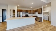 Located at 1220 W Highland Blvd in Lincoln, Nebraska, this single-floor, 2-bedroom, 2-bathroom residence offers a thoughtfully designed layout with contemporary finishes throughout. The open-concept kitchen and living area serves as the heart of the home, anchored by a generous island with a light-toned countertop, rich dark wood cabinetry, light hardwood-style flooring, and a full suite of stainless steel appliances including a refrigerator, range, microwave, and dishwasher. Recessed lighting illuminates the space, enhancing its clean, modern aesthetic. The primary bedroom features sliding glass doors that open to a private balcony with open outdoor views, while a well-appointed en-suite bathroom provides convenient access to a dedicated walk-in closet. The second bedroom is carpeted and filled with natural light from a large window, complemented by a ceiling fan overhead. Both bathrooms are finished with wood-toned vanities, marble-style countertops, and light vinyl plank flooring. The second bathroom includes a full tub-shower combination. Neutral wall tones and consistent finishes throughout create a cohesive and welcoming ambiance across every room.