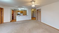 This single-floor unit offers a practical and well-organized layout with a clear separation between living, sleeping, and utility spaces. The living area is generously proportioned, featuring neutral carpet, ceiling fan with light fixture, baseboard heating, a wall-mounted air conditioning unit, and a glass-paneled entry door that allows natural light to filter in from outside.

The kitchen is designed in a galley style with warm oak cabinetry, light-toned countertops, hardwood-style flooring, a double basin sink, and white appliances including a refrigerator and range. A pass-through counter connects the kitchen to the living space, creating an open, communicative flow. A separate door within the kitchen leads to additional storage or utility space.

Two carpeted bedrooms each include ceiling fans and neutral walls, with one featuring a window with blinds and a wall-mounted air conditioner. Closet access is visible from both rooms.

Two bathrooms serve the unit. The full bathroom includes a tub-shower combination with tile surround, an oak vanity with light-colored countertop, a lighted mirror, and tile flooring. A second bathroom provides a standalone shower stall with white tile walls and chrome fixtures. The overall ambiance is clean, neutral, and move-in ready.