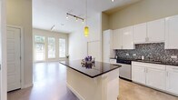 This single-floor space showcases a contemporary design highlighted by soaring ceilings and polished concrete floors that run throughout, creating a sleek, cohesive aesthetic. The open-concept layout connects the kitchen and living areas seamlessly, making the space feel expansive and airy.

The kitchen is well-appointed with crisp white cabinetry extending to the ceiling, dark granite countertops, and a striking mosaic tile backsplash featuring metallic tones. A central island with a matching dark countertop provides additional prep and gathering space. Stainless steel appliances, including a range, microwave, refrigerator, and dishwasher, complete the functional and stylish kitchen.

The living area benefits from tall ceilings and large windows alongside a glass-paneled exterior door, allowing generous natural light and outdoor views. Track lighting offers additional illumination throughout the main living space.

The bedroom is a calm, bright retreat with large windows that frame outdoor greenery and polished concrete floors continuing the home's consistent design language.

The bathroom features a dual-sink vanity topped with marble-patterned countertops, white cabinetry, a large mirror, and access to a walk-in closet, combining practicality with refined finishes throughout.