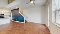 Located at 4815 Market Green Place West in Lakeland, TN, this three-story home offers three bedrooms, two bathrooms, and a well-designed layout spread across three distinct floors. The main level features a bright, open-concept living and kitchen area with soaring ceilings that amplify the sense of space. The kitchen is outfitted with white cabinetry, granite countertops, stainless steel appliances including a refrigerator, microwave, and range, and a peninsula with a built-in sink — all illuminated by stylish pendant lighting. Rich hardwood-style flooring flows throughout all levels, adding warmth and continuity. A staircase with dark wood treads and a white railing connects the floors with visual contrast. The upper levels house the three bedrooms, each featuring ceiling fans, generous natural light from multiple windows, and hardwood-style flooring. The spacious primary bedroom includes a walk-in closet. Two bathrooms serve the home — one with a tub-shower combo and built-in shelving, and another en-suite with a standalone glass-enclosed shower, granite vanity, and white cabinetry. The clean, neutral palette and modern finishes throughout create a bright, move-in-ready ambiance.