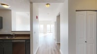 This single-floor residence is thoughtfully designed to maximize natural light and urban views. A welcoming entry hallway with light wood-style flooring leads into the main living area, where expansive floor-to-ceiling windows frame sweeping city views and flood the space with sunlight. The open-concept living area is generously proportioned, with neutral-toned walls, textured ceilings, and consistent light hardwood-style flooring throughout, creating a bright and cohesive atmosphere. A sliding glass door provides access to an outdoor balcony area, further enhancing the connection to the surrounding cityscape.

The kitchen is well-appointed with grey cabinetry, granite-style countertops, and stainless steel appliances including a range, over-the-range microwave, and dishwasher. Track lighting overhead adds a functional yet modern touch. The bedroom features plush carpeting, generous closet space with bifold doors, and lofty ceilings that contribute to an airy feel. The bathroom is finished with white cabinetry, a tile-surround tub and shower combination accented with neutral earth-toned tile banding, and a clean white vanity with an undermount sink. Overall, the space offers a clean, contemporary aesthetic with practical finishes throughout.