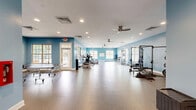 Located at 1000 Willow Oak Ln in Jackson, Tennessee, this fitness and recreation facility offers a generously sized, single-floor exercise space designed to accommodate a wide range of physical activities. The interior is defined by its striking light blue walls, crisp white ceilings, and durable speckled flooring — a combination that creates a clean, energizing atmosphere throughout.

The open floor plan is thoughtfully organized to serve multiple fitness purposes. Cardio equipment, including treadmills, ellipticals, and stationary bikes, is positioned near large multi-pane windows that flood the space with natural light and provide views of the surrounding outdoor area. A dedicated strength training zone features a power rack and free weights, while a separate area accommodates table tennis, offering recreational variety alongside traditional fitness activities.

Recessed lighting and ceiling fans are distributed throughout the space, ensuring consistent illumination and airflow. The abundant windows along multiple walls amplify the sense of openness and keep the environment well-ventilated and inviting. A whiteboard mounted on one wall supports class scheduling or instructional use, suggesting the space is well-suited for group fitness programming. The layout's generous proportions allow for flexible use, making this facility an ideal all-in-one destination for both structured workouts and active recreation.