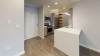This well-appointed single-floor residence offers a thoughtfully designed layout with modern finishes throughout. The open-concept living and dining area features dark hardwood-style flooring, neutral gray walls, crown molding, and recessed lighting, creating a bright and welcoming atmosphere. Large windows allow natural light to fill the space generously.

The kitchen is equipped with stainless steel appliances, including a gas range, over-the-range microwave, and French door refrigerator. Gray flat-front cabinetry pairs with white quartz countertops, and a built-in open wood shelving unit adds both storage and visual warmth. A peninsula with a sink and additional seating space connects the kitchen seamlessly to the living area.

Both bedrooms are finished with plush wall-to-wall carpeting and feature windows with blinds that invite natural light. The rooms offer a clean, neutral palette suitable for a variety of furnishing styles.

The unit includes two full bathrooms. The primary bathroom features a floating gray vanity with a backlit mirror and integrated white sink, alongside a tub-shower combination and dark wood-style flooring. The secondary bathroom offers a similar tub-shower setup with a grab bar, wood-style flooring, and chrome fixtures. The overall design is clean, contemporary, and move-in ready.