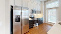 Located at 531–599 S Dillard St in Durham, NC, this single-floor residence combines contemporary design with practical functionality throughout its well-organized layout. The entryway welcomes residents with warm hardwood-style flooring, crisp white five-panel doors, and a built-in nook with shelving and a bench — a convenient drop zone upon arrival.

The kitchen is a standout feature, showcasing floor-to-ceiling white shaker cabinetry, dark lower cabinets, and a clean white countertop island with an undermount sink. Stainless steel appliances — including a side-by-side refrigerator with ice and water dispenser, an electric range, and an over-the-range microwave — complete the space. Pendant lighting and a nearby window allow natural light to brighten the area.

The bedroom offers plush carpeting underfoot and a generously sized closet with a full-length hanging rod, accessed through a classic five-panel door. The bathroom is finished with neutral tones, featuring a dual-sink dark vanity with a white quartz countertop, a large framed mirror, and a soaking tub/shower combination accented by white subway tile. The overall ambiance throughout is clean and modern, with a cohesive palette of warm neutrals, white trim, and dark accents that lend the space a polished, move-in-ready character.