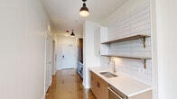Located in the Uptown neighborhood of Chicago, this single-floor unit at 1133 W Lawrence Ave offers a clean, modern aesthetic defined by thoughtful design and high-quality finishes throughout. The polished concrete floors extend seamlessly across the entire space, reflecting natural light and lending an industrial-chic character to every room.

The kitchen is efficiently laid out and well-appointed, featuring warm wood cabinetry, white quartz countertops, a stainless steel sink, and a subway tile backsplash that extends to the ceiling. Open shelving with wood brackets adds both functionality and visual depth, while matte black pendant lighting provides focused illumination. A stainless steel range and refrigerator complete the culinary space.

A hallway connects the kitchen to the remaining rooms, maintaining a logical and open flow throughout the unit. The living and sleeping areas are bright and airy, each benefiting from large, dark-framed windows that frame sweeping elevated views of the Chicago skyline and the city's street grid below — a standout feature of this space.

The bathroom is finished with floor-to-ceiling white tile and equipped with a walk-in shower featuring matte black fixtures, a rainfall showerhead, and a handheld sprayer, conveying a clean, spa-like atmosphere. The overall design palette of white walls, warm wood tones, and black accents creates a cohesive and contemporary living environment.
