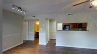 This single-floor residence offers a thoughtfully designed open-concept layout that promotes a natural flow between living spaces. The interior is anchored by rich, dark hardwood flooring that extends throughout, lending a warm and cohesive aesthetic to the entire space.

The kitchen is positioned at the heart of the home, featuring warm-toned wooden cabinetry, dark granite-style countertops, and a peninsula that opens directly to the main living area — ideal for casual dining or entertaining. Built-in appliances, including a microwave, are neatly integrated into the cabinetry.

The living area is bright and spacious, with neutral light grey walls that complement the flooring and create a versatile backdrop for any décor style. Track lighting adds a modern touch and ensures excellent illumination throughout. Ceiling vents suggest a centralized climate control system for year-round comfort.

A hallway leads to additional rooms, including what appears to be a well-lit bedroom or bathroom, offering privacy from the main living spaces. A closet with louvred bifold doors provides convenient built-in storage. White trim and clean architectural lines throughout contribute to a polished, move-in-ready feel. Overall, the space balances practicality with a clean, contemporary character.