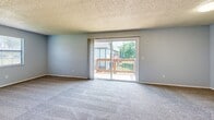 Located at 8700 Buckingham Lane in Kansas City, MO, this single-floor unit offers three bedrooms, one bathroom, and a practical, well-organized layout. The living area features plush carpeting and a textured ceiling, with a sliding glass door that opens to a private wooden deck overlooking green outdoor surroundings, filling the space with natural light. The generously sized primary bedroom is notably spacious, complete with a dedicated walk-in closet outfitted with dual hanging rods and light wood-style flooring — providing ample storage. The two additional bedrooms each feature soft carpeting, neutral gray walls, textured ceilings, and windows that bring in natural light. The kitchen is equipped with white cabinetry, granite-style countertops, and light wood-look flooring, offering a clean and functional workspace. A hallway connects the main areas of the unit, contributing to efficient traffic flow. The bathroom includes a tiled tub-shower combination with chrome fixtures, maintaining a clean and classic aesthetic. Throughout the unit, a consistent palette of soft gray walls, white trim, and textured ceilings creates a cohesive and understated character suited for comfortable everyday living.