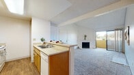 Located in La Mesa, California, this single-story unit offers a practical and open interior layout designed for comfortable everyday living. The living room serves as the central gathering space, featuring vaulted ceilings that lend a sense of openness, plush carpeting, and a fireplace with a tiled surround as a focal point. A sliding glass door connects the living area directly to an outdoor space, allowing natural light to flow in and providing easy access to exterior views.

The kitchen is positioned adjacent to the living room and is defined by a peninsula counter that creates a natural division between the two spaces while maintaining an open, connected feel. Warm wood-toned cabinetry provides ample storage, complemented by light countertops, a double sink, a dishwasher, and a coil-top electric range with an overhead ventilation hood. The kitchen floor features wood-style flooring, contrasting with the carpeted living areas.

The bedrooms are carpeted and bright, each receiving natural light through windows with vertical blinds. The bathroom includes a wide vanity with warm wood cabinetry, a large mirror, overhead lighting, and wood-style flooring, offering a clean and functional space. Overall, the unit presents a neutral, light-filled interior throughout.