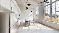 This thoughtfully designed loft-style residence blends industrial character with modern finishes throughout. The open-concept living and kitchen area commands attention with dramatic vaulted ceilings clad in whitewashed wood planking, polished concrete floors, and oversized arched windows that flood the space with abundant natural light. The kitchen is well-appointed with crisp white shaker cabinetry, subway tile backsplash, granite countertops, a full suite of stainless steel appliances, and a central island with a tiled top — all beneath a striking row of pendant lights. A ceiling fan anchors the living area, adding to the airy, loft-inspired ambiance. The spacious bedroom features soaring ceilings, a ceiling fan, and direct access to a private en-suite bathroom finished with sage-green cabinetry, granite countertops, a framed mirror, and black hardware accents. A second full bathroom includes a tub/shower combination and matching upscale finishes. The hallway leads to two closets, offering ample storage, and is accented by a stylish sliding barn door. A dedicated laundry room houses a full-size Whirlpool washer and dryer, adding everyday convenience to this well-equipped, character-rich space.