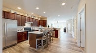 Located at 5322 Sanctuary Ln in Sheffield, Ohio, this single-story home offers a thoughtfully designed open-concept layout that promotes seamless flow between living spaces. Light wood-look luxury vinyl plank flooring runs throughout the main living areas, complementing the neutral warm-toned walls and crisp white trim and door details visible throughout.

The kitchen serves as the heart of the home, showcasing rich dark cherry cabinetry extending to the ceiling, stainless steel appliances including a range, dishwasher, and refrigerator, and a granite-topped center island with seating for multiple guests. Recessed lighting illuminates the space, which opens directly into a comfortable living area complete with a ceiling fan and access to natural light from large windows.

The primary bedroom features plush carpeting, generous natural light from a large window with outdoor views, and direct access to a private en-suite bathroom. The en-suite includes a walk-in glass shower, granite vanity countertop, and rich cabinetry. A second full bathroom mirrors the same quality finishes with a granite vanity and wood-look flooring.

The living room provides an inviting retreat with neutral tones and ample space for comfortable furnishings, creating a cohesive and functional home overall.