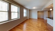 This 1-bedroom, 1-bathroom unit offers a thoughtfully designed single-level layout that balances comfort and functionality. The open living area is finished with warm-toned hardwood flooring that extends throughout the main living spaces, complemented by neutral taupe walls and multiple windows that invite natural light and frame urban cityscape views. The kitchen is a standout feature, showcasing dark espresso cabinetry, dark granite countertops, and a suite of black appliances including a range, microwave, and refrigerator. A peninsula with a stainless steel sink and pendant lighting overhead adds a modern touch while creating a natural division between the kitchen and living area. Recessed lighting provides additional illumination throughout the kitchen. The bedroom is carpeted for comfort and features a large window overlooking the surrounding cityscape, creating a bright and airy retreat. The bathroom is finished with large-format dark tile flooring and includes a clean, modern walk-in shower with a sliding glass door and recessed lighting. The entryway is practical and welcoming, providing a clear transition into the living and kitchen areas. Overall, the unit presents a clean, contemporary aesthetic with durable finishes suited for urban living.