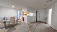 This single-floor residence offers a thoughtfully designed layout that balances comfort and functionality throughout. The open-concept living and dining area is anchored by soft carpeting and natural light filtering through slatted blinds, creating a bright and welcoming atmosphere. The living room features a coastal-inspired aesthetic, complete with neutral tones and a charming anchor wall accent. The adjacent dining area includes a glass-top table and access to a patio through a sliding door dressed in vertical blinds.

The galley-style kitchen is well-equipped with warm wood cabinetry, granite-look countertops, light wood-style flooring, and full appliances including a refrigerator and electric range. Two bathrooms mirror each other in style, each featuring rich wood vanities topped with speckled granite counters and wood-look tile flooring.

The primary bedroom makes a bold impression with a deep navy accent wall, a ceiling fan, carpeted flooring, and a window that invites in natural light. A second bedroom carries the same navy palette and ocean-themed artwork, while a third room — ideal as a children's bedroom — features a soft blue accent wall, ceiling fan, carpeted floors, and a window overlooking greenery outside.