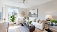 This thoughtfully designed single-floor residence offers a cohesive layout encompassing a living room, kitchen, bedroom, bathroom, closet, and hallway. The open-concept kitchen is a standout feature, showcasing crisp white shaker cabinetry, a white subway tile backsplash, quartz countertops, stainless steel appliances, and a central island with seating — all set atop light-toned hardwood flooring that flows throughout the main living areas. The living room is bright and welcoming, featuring a ceiling fan, large sliding windows that invite abundant natural light, and direct views of the surrounding urban landscape. The bedroom offers a comfortable, carpeted retreat with generous windows framed by floor-to-ceiling drapes, providing both natural light and city views. A dedicated closet provides convenient storage adjacent to the bedroom. The bathroom is clean and modern, finished with a white vanity, full tub with shower, and light wood-tone flooring consistent with the rest of the unit. Neutral tones, recessed lighting, and clean architectural lines are carried throughout, creating a cohesive, contemporary ambiance that feels open and airy despite its efficient footprint.