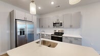 Located at 8067 Purchase Pl NE in Leland, NC, this thoughtfully designed one-bedroom, one-bathroom residence offers a clean, contemporary aesthetic with an efficient, well-organized layout. The open-concept kitchen and living area serves as the heart of the home, where a sleek kitchen island with a stainless steel sink and white quartz countertops anchors the space. The kitchen is outfitted with gray flat-front cabinetry, a white subway tile backsplash, stainless steel appliances including a French door refrigerator and electric range, and pendant lighting overhead. Wood-look plank flooring flows seamlessly throughout, lending warmth and visual continuity. The living area extends from the kitchen toward a large window, filling the space with natural light and providing views of the surrounding neighborhood. The bedroom is a comfortable, well-proportioned retreat featuring a ceiling fan, a window with exterior views, and access to a dedicated closet with wire shelving for organized storage. The bathroom is finished with a white vanity offering ample cabinet and drawer storage, a large mirror, and wood-look tile flooring. The overall ambiance is bright, clean, and move-in ready, reflecting modern residential design throughout.