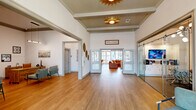 Located at 691 Union Chapel Rd in Cedar Creek, TX, this single-floor commercial space offers a well-designed layout that balances openness with functional, defined areas. The main reception and lobby area makes a strong first impression with soaring ceilings, warm wood-plank flooring, and a tongue-and-groove wood ceiling accented by striking sunburst light fixtures. Exposed beams add architectural character, while large glass entry doors flood the space with natural light and provide views of the surrounding exterior. A reception desk with seating areas is positioned to welcome visitors, with wall art and decorative accents adding warmth to the professional environment. A glass-walled conference or workspace area sits adjacent to the main hall, offering visibility and connectivity while maintaining a sense of separation. This room features a wall-mounted display and built-in white cabinetry, making it well-suited for presentations or client meetings. A more intimate private meeting room with carpeted flooring, a solid wood table, upholstered chairs, and framed artwork provides a quiet, focused setting. The overall design blends modern commercial functionality with inviting, tasteful décor, creating a professional yet approachable atmosphere throughout.