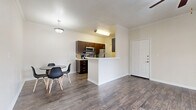 Located at 1900 Aquarena Springs Dr in San Marcos, TX, this single-floor, 3-bedroom, 2-bathroom home offers a practical and well-appointed layout. The open-concept living, dining, and kitchen area forms the heart of the home, featuring durable wood-look flooring, crown molding, and a ceiling fan with light fixture. The kitchen is equipped with stainless steel appliances — including a refrigerator, range, and microwave — rich dark-brown cabinetry, a tile backsplash, and a peninsula with an integrated sink that doubles as a breakfast bar. The dining area comfortably accommodates a table and chairs beneath a pendant light. Two of the three bedrooms are finished with plush carpet and ceiling fans, each featuring a window that brings in natural light. The third bedroom features wood-look flooring. The bathrooms include dark-wood vanities with light countertops, wood-look tile flooring, and a full tub-shower combination. A dedicated laundry room provides washer and dryer hookups with overhead shelving. Five closets throughout the home offer generous storage. The covered patio provides outdoor seating and views of the surrounding tree-lined neighborhood. A hallway connects the private quarters seamlessly to the main living space.