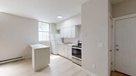 Located at 30 Black Creek Rd in Esopus, NY, this two-story home offers a thoughtfully designed layout across two levels. The main floor hosts the open-plan living, dining, and kitchen area, finished with light hardwood-style flooring that creates a clean, airy feel throughout. The kitchen is well-appointed with white shaker cabinetry, a subway tile backsplash, a stainless steel range, and a central island featuring a marble-look countertop — ideal for both cooking and casual dining. A window brings in natural light, enhancing the bright, neutral palette of the space. The living area benefits from dramatic vaulted ceilings with exposed wood beam accents, adding architectural character and a sense of openness that belies the home's compact footprint. A staircase leads to the upper level, where the two bedrooms are situated, including a generously sized primary bedroom. Three closets are distributed throughout the home, providing practical storage. The full bathroom features a tub-shower combination with a handheld showerhead and a clean, all-white finish with gold hardware accents. The home's consistent use of light tones and modern finishes gives it a fresh, move-in-ready appearance throughout.
