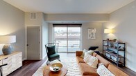 This thoughtfully designed single-floor residence offers a seamless blend of modern aesthetics and functional living. The open-concept kitchen is a standout feature, showcasing crisp white cabinetry, stainless steel appliances including a gas range, microwave, dishwasher, and refrigerator, complemented by a dark subway tile backsplash and warm wood open shelving. An industrial-style pendant light fixture anchors the kitchen island, which doubles as a breakfast bar with quartz-style countertops and hardwood flooring underfoot.

The living area flows naturally from the kitchen, bathed in natural light through large sliding glass doors that open to a balcony with expansive urban views. The bedroom is a serene retreat, highlighted by a striking textured accent wall, plush carpeting, a ceiling fan, and a generous window that frames city views.

The full bathroom is clean and well-appointed, featuring a tub-shower combo with tile surround, a wide white vanity with black hardware accents, and hardwood-style flooring. A dedicated laundry area with a stacked washer and dryer adds everyday convenience. Neutral tones throughout create a cohesive, welcoming ambiance across the entire space.