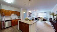 This well-appointed two-bedroom, two-bathroom residence at 10 Glenbrook Rd in Stamford, Connecticut, offers a thoughtfully designed single-floor layout with elegant finishes throughout. The open-concept kitchen is a standout feature, showcasing rich warm-toned cabinetry, granite countertops, a central island with pendant lighting overhead, and a full suite of stainless steel appliances including a refrigerator, gas range, microwave, and dishwasher. Subway tile backsplash and hardwood-style flooring complete the kitchen's refined aesthetic. The kitchen flows seamlessly into the dining and living areas, which are carpeted and finished with classic crown molding, creating a cohesive and comfortable gathering space. Large windows allow natural light to fill the living room, which features direct access to an exterior door. The primary bedroom is generously sized with plush carpeting and a walk-in closet. The second bedroom offers flexible use as a home office or guest room. Both bathrooms are clean and well-finished, each featuring a tub-shower combination with tiled surrounds and white vanities. A walk-in closet off the kitchen hallway provides additional storage. The overall ambiance is warm, classic, and move-in ready.