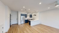 This thoughtfully designed two-story home offers three bedrooms and three bathrooms across two well-proportioned floors. The main level provides a generous open-concept layout where the kitchen and living room flow seamlessly together, creating an inviting space for both daily living and entertaining. The kitchen is a standout feature, showcasing bold navy-blue shaker cabinetry, stainless steel appliances including a gas range and French door refrigerator, a sleek wall-mounted range hood, subway tile backsplash, and a peninsula with a white quartz countertop and pendant lighting overhead. Light wood-tone flooring runs throughout, complementing the bright white walls and recessed lighting that keep the space feeling fresh and airy. The main level entry is welcoming, with a dark-framed front door and a staircase leading to the upper floor. Upstairs, the three bedrooms are well-sized, each featuring ceiling fans, natural light through windowed views of the surrounding neighborhood, and the same warm hardwood-style flooring. The primary bedroom offers a comfortable and spacious retreat. The bathrooms are clean and modern, with one featuring a tub-shower combination with subway tile surround. A dedicated laundry room with side-by-side washer and dryer adds everyday convenience, while a closet with built-in shelving and hanging rods provides ample storage throughout the home.