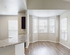 Unit #1305 at Bell Starwood in Frisco, TX is a well-appointed 2-bedroom, 2-bathroom residence spanning 1,190 square feet across two floors. The main living area features warm wood-look flooring, crown molding, soaring ceilings, and a ceiling fan, creating an open and airy atmosphere. An elegant arched doorway connects the living room to the rest of the unit, while a bay window floods the space with natural light near the entry. The kitchen is equipped with dark espresso cabinetry, granite countertops, a subway tile backsplash, stainless steel appliances including a refrigerator, range, and microwave, complemented by durable wood-look flooring. Both bedrooms are carpeted and include ceiling fans with natural light from large windows. The primary bedroom measures 180 square feet. Each bathroom features dark wood vanities with granite countertops and a tub-shower combination. The spacious walk-in closet offers wire shelving on multiple walls. A dedicated laundry room includes an in-unit washer and overhead wire shelving. A staircase connects the ground-level entry to the main living floor above, with three hallways providing efficient circulation throughout the unit.
