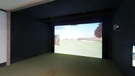 This single-floor space is purpose-built as a private indoor golf simulator room, offering an immersive experience for golf enthusiasts regardless of season or weather. The room is finished in deep, dark-toned walls that minimize light reflection and maximize the visual impact of the large projection screen dominating the far wall. The screen delivers crisp, full-width imagery of realistic golf course environments, complete with fairways, sand bunkers, and tree lines, creating a convincing and engaging simulation experience. Recessed ceiling lighting provides subtle, controlled illumination without interfering with screen visibility. The flooring is fitted with a smooth, low-pile surface appropriate for a simulator setup, offering a stable stance for players. Exposed structural beams along the ceiling add an architectural element to the otherwise minimalist interior. The overall ambiance is focused and functional — a darkened, distraction-free environment engineered specifically for golf simulation. Whether used for serious practice, game improvement, or recreational play, this space provides a well-appointed and dedicated venue for enjoying the game of golf in a fully controlled indoor setting.
