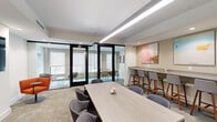 Located at 1700-1706 N Howard St in Philadelphia, PA, this thoughtfully designed single-floor workspace offers a refined and functional environment suited for collaboration and focused work. The space is organized into a welcoming lounge area and a dedicated office section, seamlessly connected through floor-to-ceiling glass-paneled partitions with sleek black framing that allow natural light to flow freely while maintaining visual separation between zones.

The main lounge and meeting area features a light wood communal table surrounded by upholstered seating, complemented by a wall-mounted counter with bar-height seating — ideal for informal meetings or individual work. A large-format abstract artwork in soft pink tones anchors the wall, adding a creative touch to the neutral palette. Recessed and linear pendant lighting ensures the space is well-lit throughout.

The glass-enclosed office rooms offer more intimate settings, each furnished with tailored seating arrangements and natural light from exterior-facing windows. A dedicated conference room provides a rectangular table with rolling chairs and a wall-mounted display screen, while a cozy lounge nook with an orange accent chair adds a casual seating option. Additional smaller meeting rooms with warm-toned seating and curated artwork complete the offering, creating a versatile, design-forward workspace.