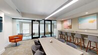 Located at 1700-1706 N Howard St in Philadelphia, PA, this thoughtfully designed single-floor workspace offers a refined and functional environment suited for collaboration and focused work. The space is organized into a welcoming lounge area and a dedicated office section, seamlessly connected through floor-to-ceiling glass-paneled partitions with sleek black framing that allow natural light to flow freely while maintaining visual separation between zones.

The main lounge and meeting area features a light wood communal table surrounded by upholstered seating, complemented by a wall-mounted counter with bar-height seating — ideal for informal meetings or individual work. A large-format abstract artwork in soft pink tones anchors the wall, adding a creative touch to the neutral palette. Recessed and linear pendant lighting ensures the space is well-lit throughout.

The glass-enclosed office rooms offer more intimate settings, each furnished with tailored seating arrangements and natural light from exterior-facing windows. A dedicated conference room provides a rectangular table with rolling chairs and a wall-mounted display screen, while a cozy lounge nook with an orange accent chair adds a casual seating option. Additional smaller meeting rooms with warm-toned seating and curated artwork complete the offering, creating a versatile, design-forward workspace.