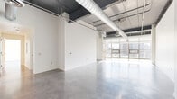 Located at 512 Reily St in Harrisburg, PA, this 3-bedroom, 2-bathroom loft-style residence offers a striking industrial-modern aesthetic across a generously sized single-floor layout. Polished concrete floors flow throughout the entire unit, reflecting natural light and contributing to the space's clean, contemporary feel. The open living areas are defined by soaring ceilings with exposed ductwork and ductwork runs, lending an authentic urban loft character. Large floor-to-ceiling windows and expansive glass panels frame views of the surrounding Harrisburg cityscape, flooding the interior with abundant natural light. A modern fireplace adds a refined focal point to the living area. The kitchen is outfitted with rich dark-stained wood cabinetry, granite countertops, stainless steel appliances including a range, microwave, dishwasher, and refrigerator, complemented by track lighting overhead. The spacious primary bedroom features tall windows with city views and access to a well-organized walk-in closet with built-in wire shelving systems. The bathrooms are finished with polished concrete floors, dual-sink vanities with dark countertops, and full soaking tubs. The layout also includes a hallway connecting the private sleeping quarters to the main living areas, offering a functional and cohesive flow throughout.