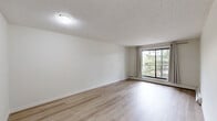 Located at 360 Falshire Drive NE in Calgary, Alberta, this 2-bedroom, 1-bathroom unit offers a practical and well-organized single-floor layout. Light hardwood flooring flows throughout the space, contributing to a clean and bright aesthetic that is consistent across all rooms.

The open living area is generously sized, featuring a textured ceiling, neutral white walls, and a large window dressed with grommet-style curtains that allow natural light to fill the room. A sliding glass door leads to a private balcony overlooking mature trees, providing a pleasant outdoor view.

The kitchen is positioned adjacent to the living area in a pass-through configuration, featuring warm wood cabinetry, light countertops, a stainless steel sink, and upper storage cabinets — offering a functional and efficient workspace.

Both bedrooms are well-proportioned and share a consistent design with light hardwood floors, textured ceilings, and large windows that frame leafy outdoor views. Each bedroom is equipped with sliding panel closets, providing ample storage.

The bathroom is clean and functional, featuring warm wood cabinetry with a white countertop vanity, a lighted mirror, and a full tiled tub-shower surround. Two hallways connect the rooms efficiently, completing this straightforward and comfortable layout.