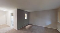 This single-floor studio features an open layout that efficiently combines living and sleeping areas into one cohesive space. The main room is finished with wall-to-wall carpeting in a neutral tan tone, complemented by gray-painted walls and crisp white trim and baseboards. A small window provides a modest source of natural light, casting a soft glow across the carpeted floor. The smooth white ceiling contributes to a clean, understated aesthetic throughout the space. The neutral color palette of gray and white creates a versatile backdrop, making the space easy to personalize with various furniture and décor styles. The single bathroom rounds out the unit, completing the functional layout. Overall, the studio presents a straightforward, move-in-ready environment well-suited for an individual seeking a compact, low-maintenance living space.