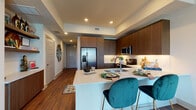 Located at 7901 Windrose Ave in Plano, Texas, this single-floor residence offers a thoughtfully designed layout with contemporary finishes throughout. A welcoming hallway with wood-look tile flooring and clean-lined panel doors sets the tone for the rest of the space.

The kitchen is a standout feature, showcasing rich dark-wood cabinetry extending to the ceiling, a full suite of stainless steel appliances including a French door refrigerator, electric range, and microwave, all complemented by quartz countertops and under-cabinet lighting. A large island with bar seating provides both additional prep space and a casual dining option.

The living area is bright and airy, benefiting from floor-to-ceiling sliding glass doors that open to a balcony with panoramic urban views of the Plano skyline. Recessed lighting and elevated ceilings enhance the sense of openness throughout the common areas.

The bedroom features plush carpeting, large windows framing expansive city views, and ample natural light. It connects directly to a well-designed en-suite bathroom complete with a glass-enclosed shower, dark wood vanity with quartz countertop, and a spacious walk-in closet. The overall ambiance is modern and refined, blending functional design with upscale finishes.