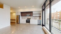 Located at 23 North Broadway Street in Tacoma, WA, this modern 1-bedroom, 1-bathroom unit showcases a clean, contemporary design throughout. The open living area is defined by striking polished concrete floors that reflect natural light pouring in through expansive floor-to-ceiling windows with black steel frames, offering views of the surrounding North Broadway neighborhood. A sliding glass door provides direct access to a balcony, further enhancing the connection to the outdoors.

The kitchen is efficiently designed with a streamlined layout featuring flat-front white lower cabinetry, dark wood upper cabinets, open floating shelves, a tiled backsplash, and a full suite of stainless steel appliances including a range, microwave, dishwasher, and refrigerator. Recessed lighting illuminates the space throughout.

The hallways are bright and well-proportioned, with multiple closets providing generous storage. The bedroom offers a carpeted floor for comfort and includes a sliding closet with built-in shelving. The bathroom is finished in a minimalist style with a long white vanity, an oversized mirror, and a tub/shower combination. The unit also features an accessible electrical panel and additional storage closets, rounding out a highly functional and modern living space.