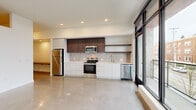 Located at 23 North Broadway Street in Tacoma, WA, this modern 1-bedroom, 1-bathroom unit showcases a clean, contemporary design throughout. The open living area is defined by striking polished concrete floors that reflect natural light pouring in through expansive floor-to-ceiling windows with black steel frames, offering views of the surrounding North Broadway neighborhood. A sliding glass door provides direct access to a balcony, further enhancing the connection to the outdoors.

The kitchen is efficiently designed with a streamlined layout featuring flat-front white lower cabinetry, dark wood upper cabinets, open floating shelves, a tiled backsplash, and a full suite of stainless steel appliances including a range, microwave, dishwasher, and refrigerator. Recessed lighting illuminates the space throughout.

The hallways are bright and well-proportioned, with multiple closets providing generous storage. The bedroom offers a carpeted floor for comfort and includes a sliding closet with built-in shelving. The bathroom is finished in a minimalist style with a long white vanity, an oversized mirror, and a tub/shower combination. The unit also features an accessible electrical panel and additional storage closets, rounding out a highly functional and modern living space.
