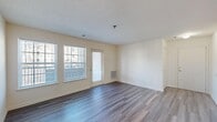 Located at 5748 Castlebridge Rd in Fredericksburg, Virginia, this single-floor residence offers a well-organized layout designed for comfortable everyday living. The main living area makes a strong first impression with durable wood-style flooring in a cool gray tone, neutral cream-colored walls, and a textured ceiling. Multiple windows along one wall allow natural light to fill the space, and a door provides direct access to the exterior. A wall-mounted thermostat and a floor-level HVAC vent indicate dedicated climate control throughout.

The galley-style kitchen is efficiently arranged with dark-finished cabinetry, light countertops, and black appliances including a full-size refrigerator and range. Overhead lighting illuminates the workspace, and the layout flows practically for meal preparation.

The bedrooms feature plush carpeting and natural light from individual windows, offering a quiet, comfortable atmosphere. One additional room with wood-style flooring and a window provides flexible use as a dining area, home office, or den.

Two bathrooms are finished with tile flooring, dark wood vanity cabinetry, light countertops, and large mirrors. A dedicated laundry area accommodates a full-size top-load washer, adding everyday convenience. Overall, the space presents a clean, functional design with consistent finishes throughout.